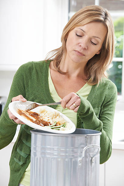istock Woman Scraping Food Leftovers Into Garbage Bin 521113383