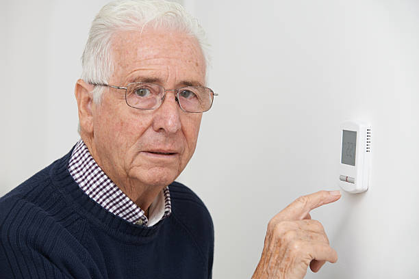 istock Worried Senior Man Turning Down Central Heating Thermostat 521113751