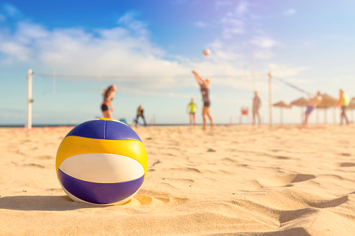 beach volleyball. ball in sands and group of people in background. focus on ball