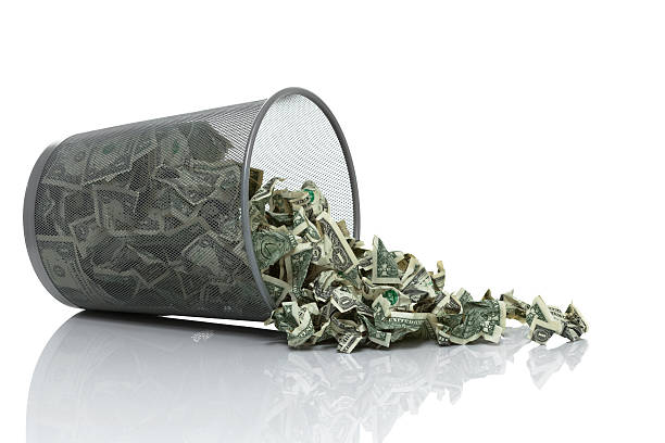 Garbage can full of money tipped on side spilling money Garbage can full of money tipped on its side with money spilling out wastepaper basket photos stock pictures, royalty-free photos & images