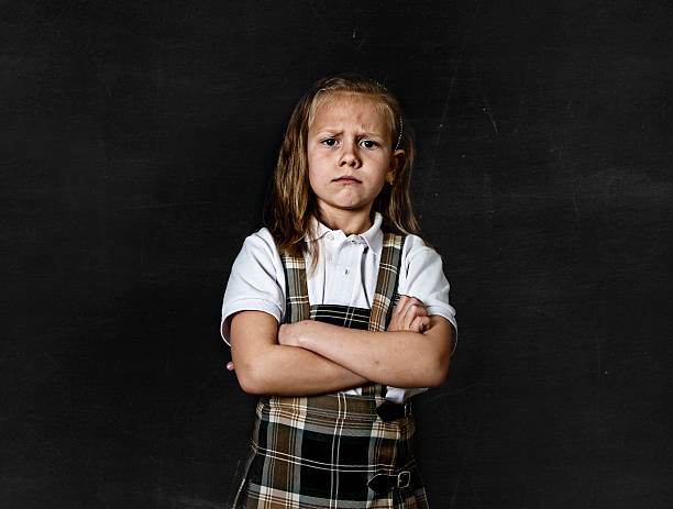 junior schoolgirl crying in children education stress and bullying victim young sweet junior schoolgirl with blonde hair moody and sad face expression standing isolated in front of blackboard with arms crossed wearing school uniform in children education stress embarrassment skirt photos stock pictures, royalty-free photos & images