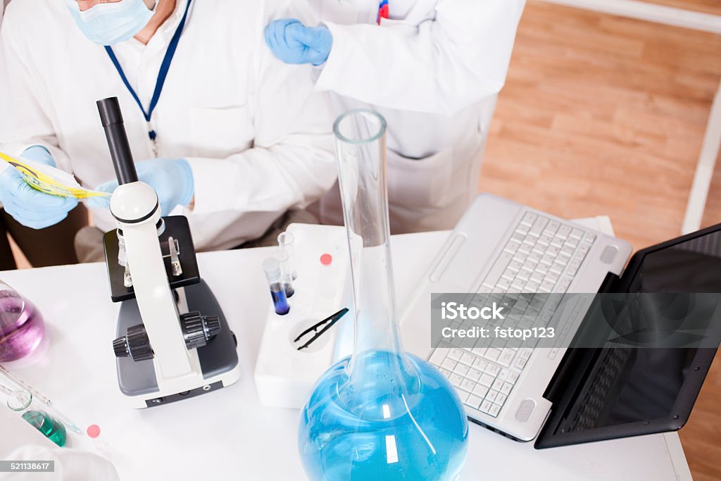 Scientists in research laboratory. Chemicals, laptop, microscope. Group of scientists working inside a research laboratory. Overhead view of scientist holding medicine bag. Microscope, laptop and chemicals. They are conducting genetic science experiments.  Above Stock Photo