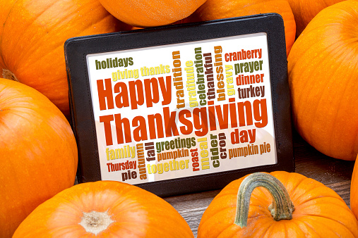 Happy Thanksgiving word cloud on a digital tablet surrounded by pumpkins