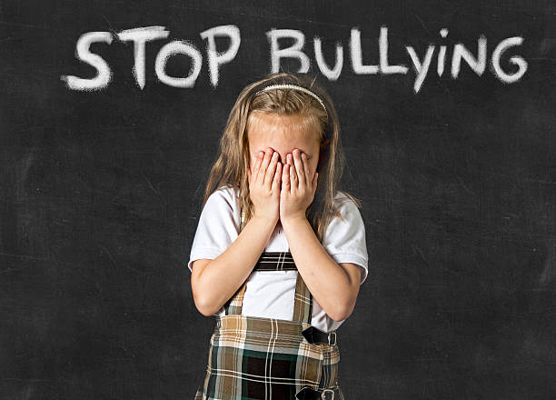 young sweet junior schoolgirl victim of school bullying crying sad young sweet junior schoolgirl victim of bully crying sad standing in front of school class blackboard with chalk text stop bullying in school children bullied and education stress embarrassment skirt photos stock pictures, royalty-free photos & images