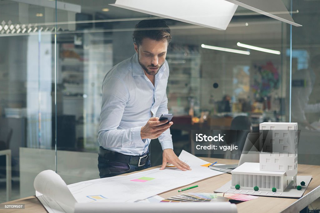 Designer typing on smart phone in office. Architect working in his office. Standing and typing on smart phone. Architect Stock Photo