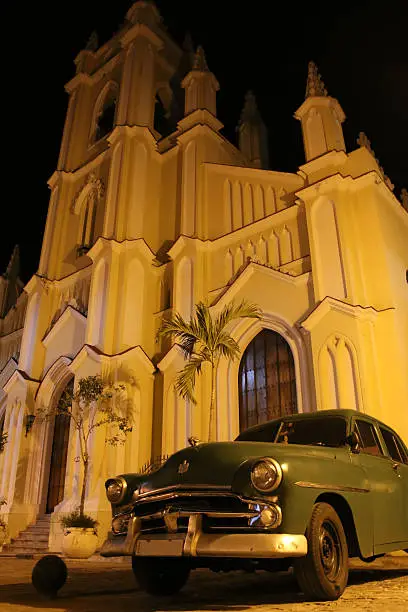 an old Cuban vintage car in front of a cathedral at night