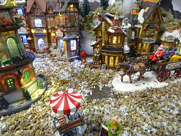 Image of model Christmas village with miniature houses, people, horse-cart Frome, Somerset, England, UK - October, 27 2014: Seasonal concept photo showing a magical model Christmas village scene set up in the conservatory of my house, using a large table, wooden staging and white polyester fleece to create a blanket of snow. The model village recreates a detailed winter's scene in miniature and comes complete with miniature ceramic buildings and houses, realistic plastic, hand-painted people and scale figurines, tiny battery-powered fairy lights (all made by Lemax) and lots of fake snow powder. covered wagon horse cart snow winter stock pictures, royalty-free photos & images