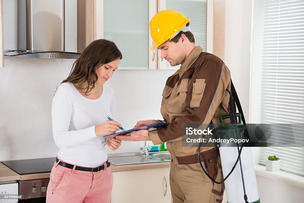 Woman Signing Document In Front Of Exterminator Young Woman Signing Document In Front Of Male Exterminator In Kitchen Exterminator Stock Photo