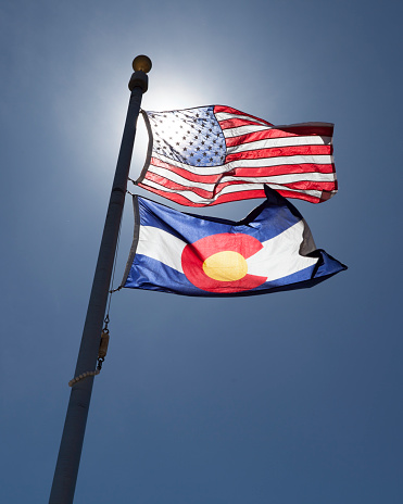 The American and State of Colorado flags flying on a sunny day