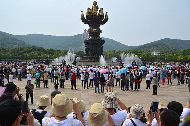 Ling Shan, China - May 24, 2014: Crowd of chinese tourists taking pictures to the Buddha's birth sculpture with a scenic dancing fountain. In the background the Grand Buddha, a 88 metres high bronze statue located at the south of the Longshan Mountain, near Wuxi, Jiangsu Province, It is one of the largest Buddha statues in the world