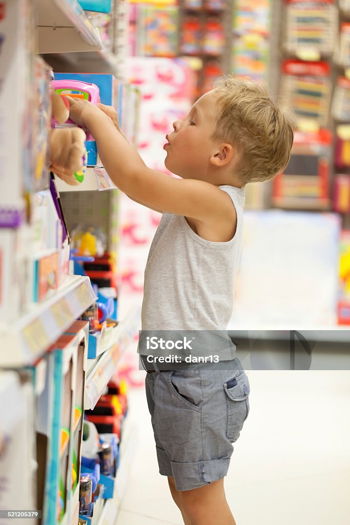 Boy choosing toy in the shop Little boy choosing toys on the high shelf in the shop Toy Store Stock Photo