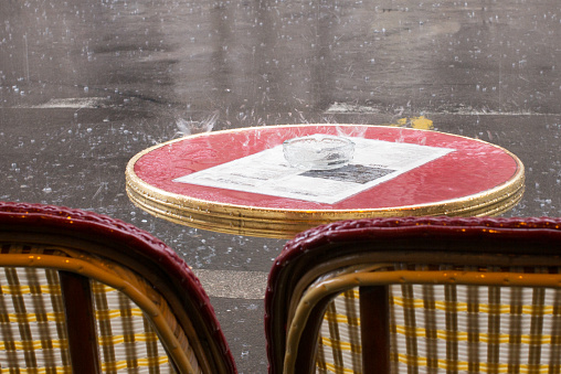 Sitting on the terrace of a parisian café on a rainy day. It is pouring, and raindrops bounce on the tables. Paris. France