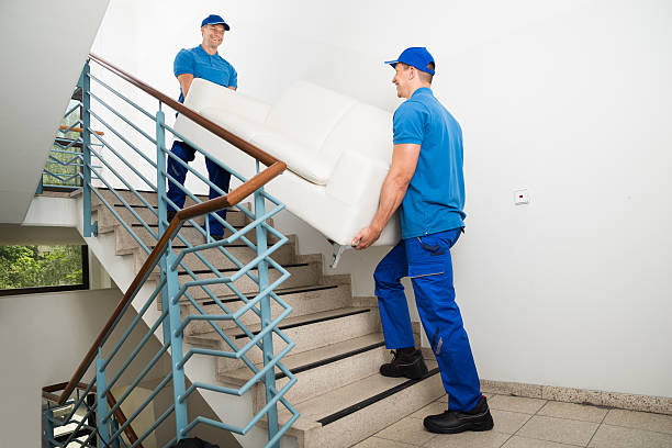 Two Happy Male Movers In Uniform Carrying White Sofa On Staircase
