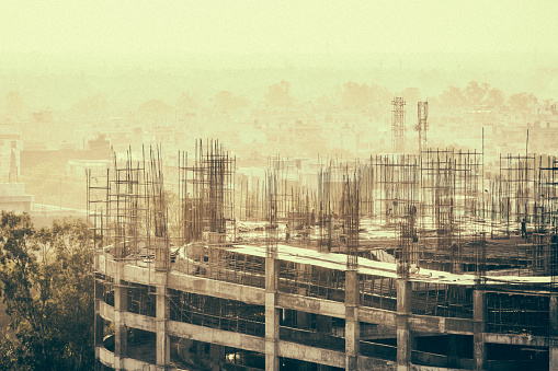 Sepia toned image of a construction site in the Janakpuri neighbourhood of New Delhi, India. Unrecognizable workers are visible in the image.