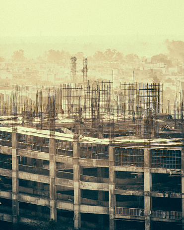 Sepia toned image of a construction site in the Janakpuri neighbourhood of New Delhi, India. Unrecognizable workers are visible in the image.