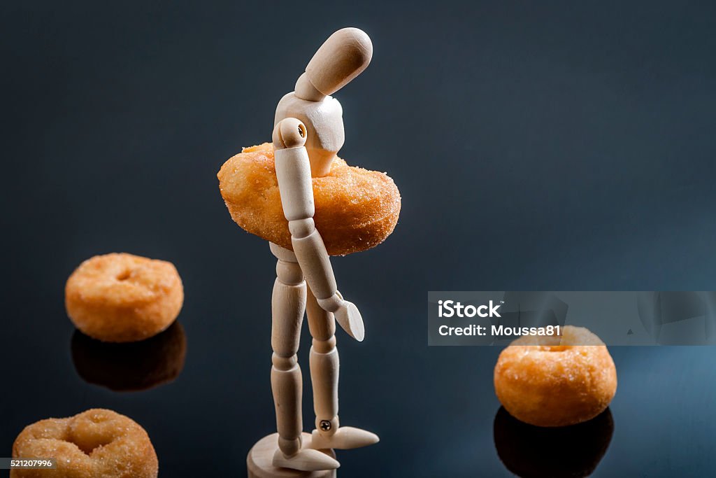 Sad and depressed overweight human figurine Human shaped figurine surrounded by doughnuts and with a doughnut around the waist made to look like the belly of a overweight person  Sugar - Food Stock Photo