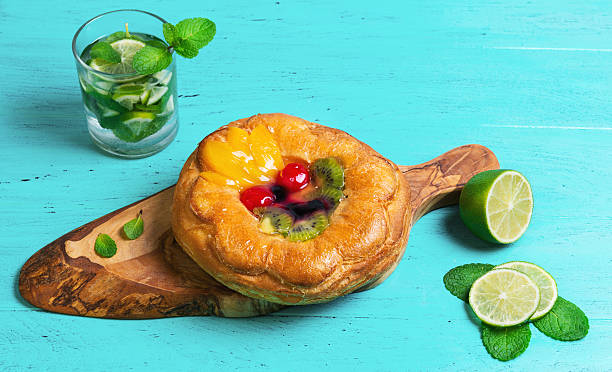 Denish fluffy bun with fruits and jelly on top Denish fluffy bun with fruits and jelly on top, a glass of mojito, sliced lime, towel napkin, on a board of wood on olive green wooden background in rustic style denish stock pictures, royalty-free photos & images