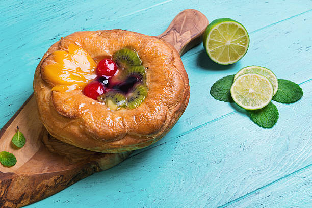 Denish fluffy bun with fruits and jelly on top Denish fluffy bun with fruits and jelly on top, liced lime, towel napkin, on a board of wood on olive green wooden background in rustic style denish stock pictures, royalty-free photos & images