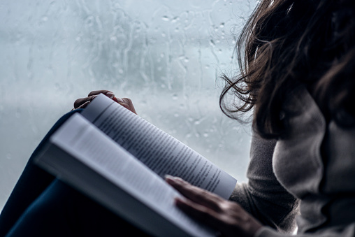 Women how Reading Book next to Window While Raining. Spending quality time while the storm.