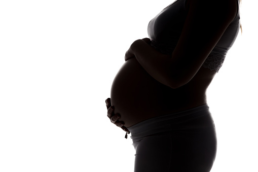 Silhouette of expectant mother in profile, hugging belly on white background
