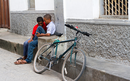 Stone Town, Zanzibar, Tanzania - May 20, 2012: Two young men looking at a cell phone in central Stone Town, with a nearby bike.