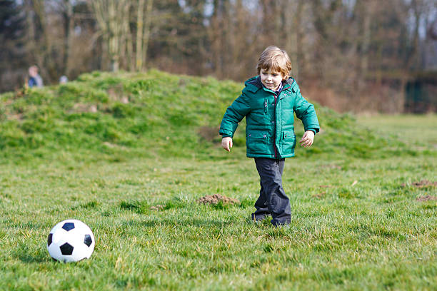 kleine junge spielen fußball oder fußball an kalten tag - playing field goalie soccer player little boys stock-fotos und bilder