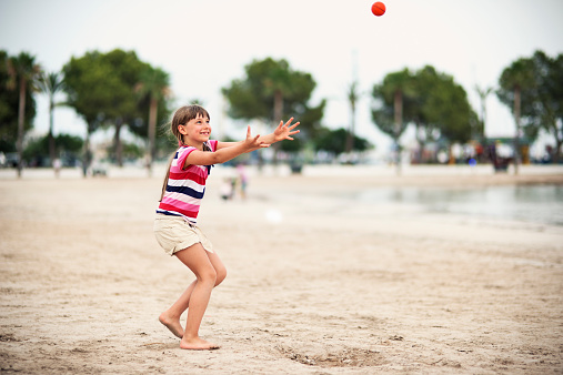 Little girl playing throw and catch with a ball on the beach.
