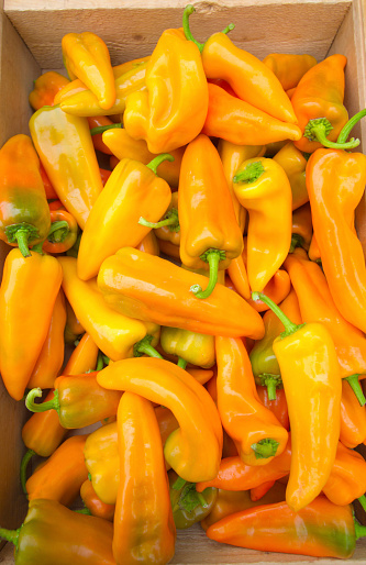 Close-up shot of a pile of orangish-yellow chili peppers in a wooden crate.