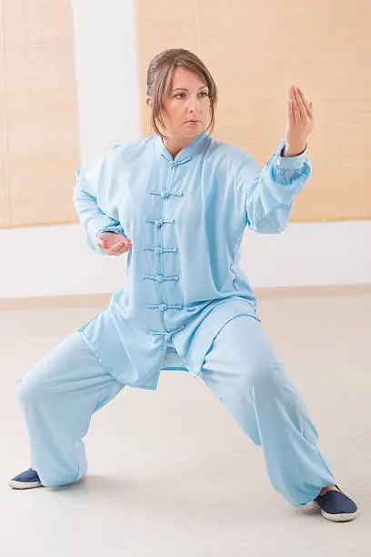 Beautiful woman doing qi gong tai chi exercise wearing professional, original Chinese clothes at gym