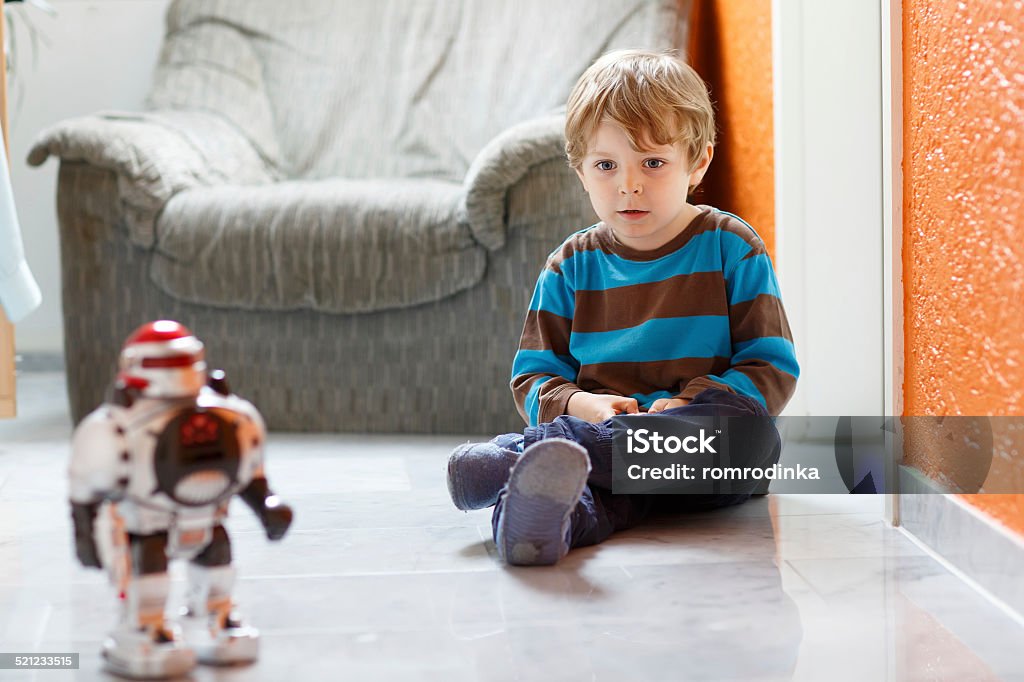 Poco niño rubia jugando con juguetes en casa, robot bajo techo. - Foto de stock de Robot libre de derechos