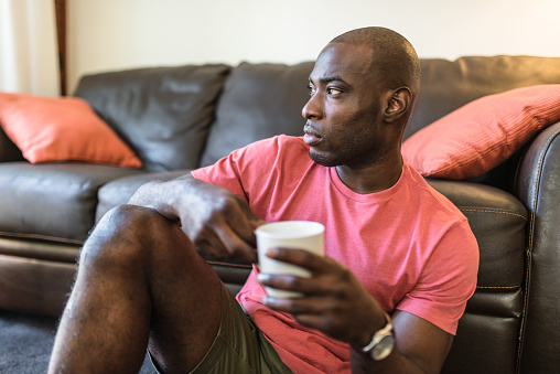 African man pensive while is drinking the coffee on the living room