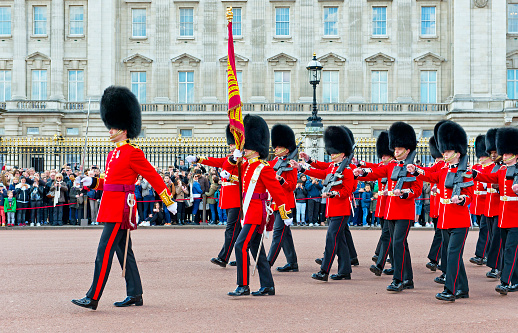 Armed soldiers guards using bearskin standing in the front yard at Buckingham Palace, London, England. This picture was taken from outside the palace during the changing of The Queen's Guard, the infantry soldiers charged with guarding the official royal residences in the United Kingdom. A bearskin is a tall fur cap, usually worn as part of a ceremonial military uniform.