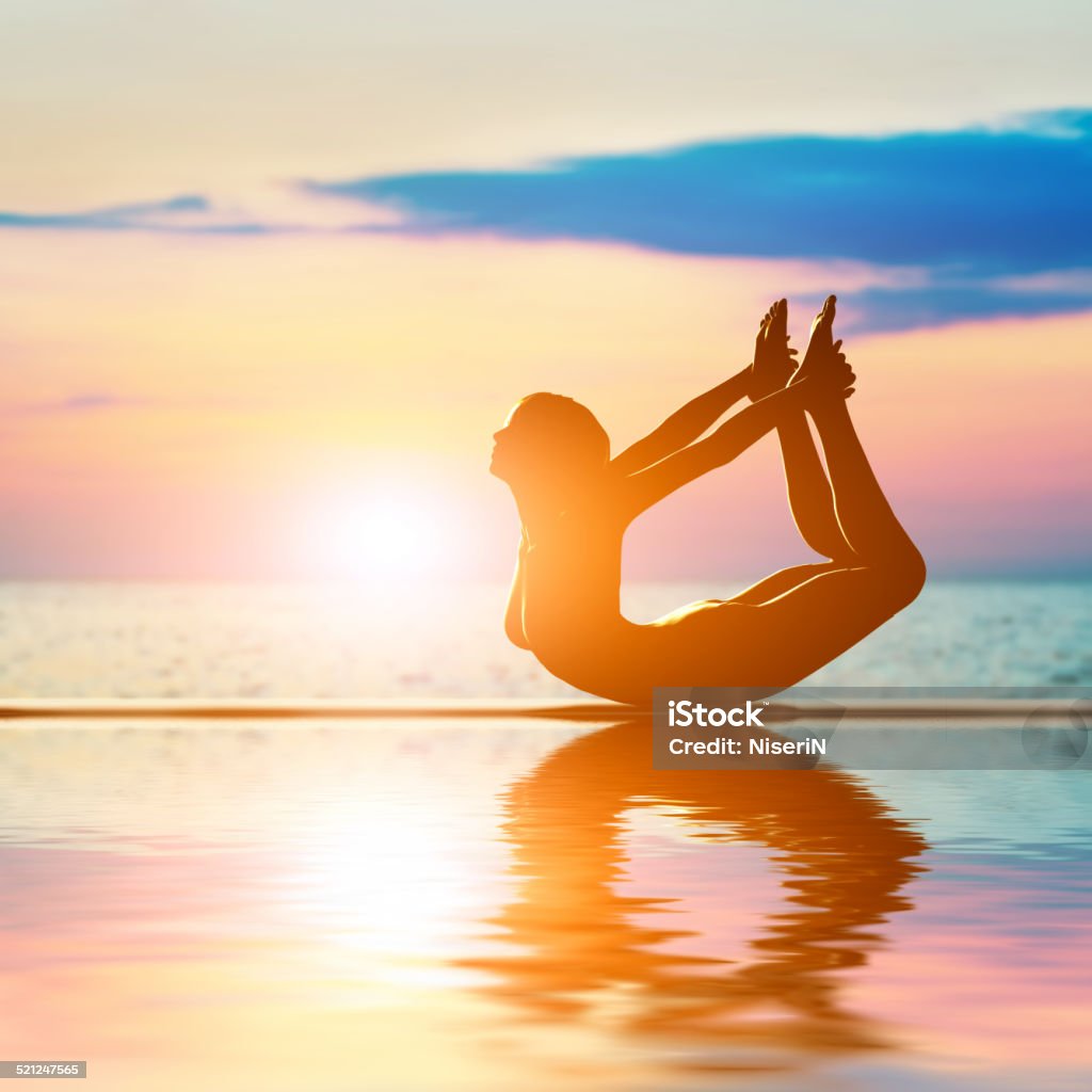 Silhouette of a woman in bow yoga position A silhouette of a woman in bow yoga position, meditating against sunset sky. Zen, meditation Adult Stock Photo