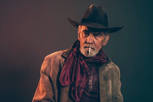 タバコの喫煙シニアカウボーイにグレイのヒゲと茶色の帽子ます。 - cowboy hat real people red gray ストックフォトと画像
