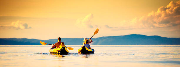 Panoramic shot of young family enjoy sea kayaking in the sunset, rear view.