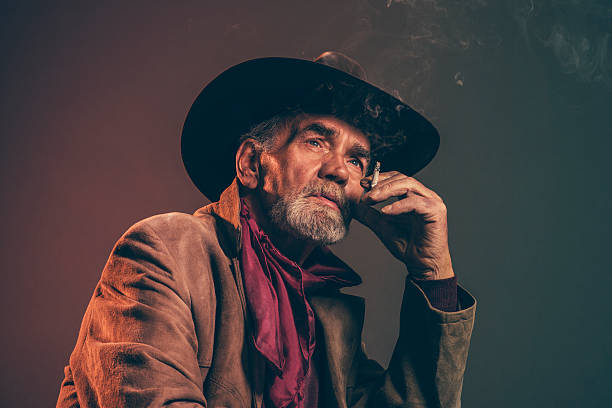 fumar cigarros com barba grisalho senior cowboy marrom e chapéu. - men hat leather senior adult - fotografias e filmes do acervo