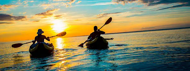 Silhouette of young family enjoy sea kayaking in the sunset, panoramic tilted shot.