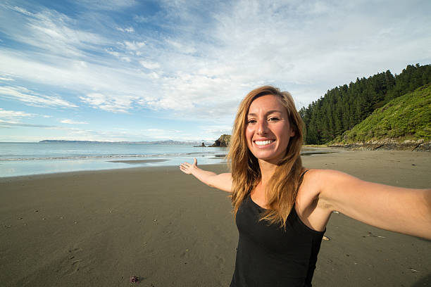 陽気な若い女性が自分撮りビーチでのポートレート - marlborough region sunrise new zealand sea ストックフォトと画像