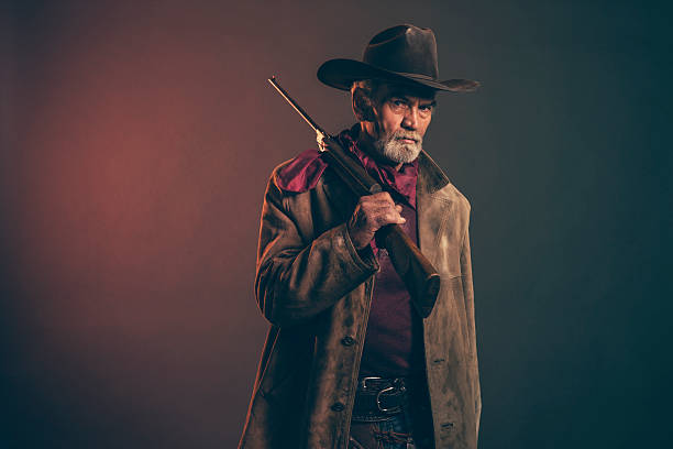 istock Senior cowboy with gray beard and brown hat holding rifle. 521262083