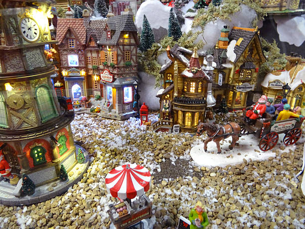 Image of model Christmas village with miniature houses, people, horse-cart Frome, Somerset, England, UK - October, 27 2014: Seasonal concept photo showing a magical model Christmas village scene set up in the conservatory of my house, using a large table, wooden staging and white polyester fleece to create a blanket of snow. The model village recreates a detailed winter's scene in miniature and comes complete with miniature ceramic buildings and houses, realistic plastic, hand-painted people and scale figurines, tiny battery-powered fairy lights (all made by Lemax) and lots of fake snow powder. covered wagon horse cart snow winter stock pictures, royalty-free photos & images