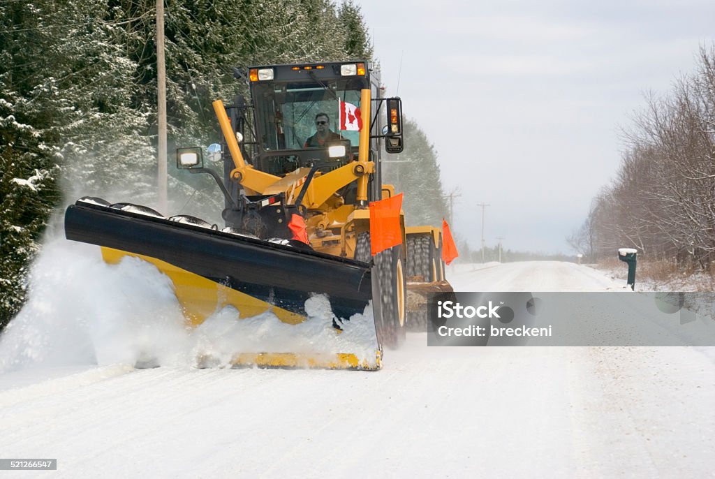 snowplowing grader - close up a grader fitted with blades and plowing the snow off a gravel road Occupation Stock Photo