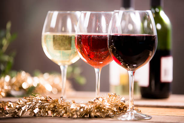 Wine, glasses on rustic outdoor dining table. Christmas tinsel. Christmas party. Wine tasting. Red, white, and rose wine selections on outdoor patio table.  Wine bottles. Rustic wooden table.  Gold tinsel holiday decor. rose christmas red white stock pictures, royalty-free photos & images