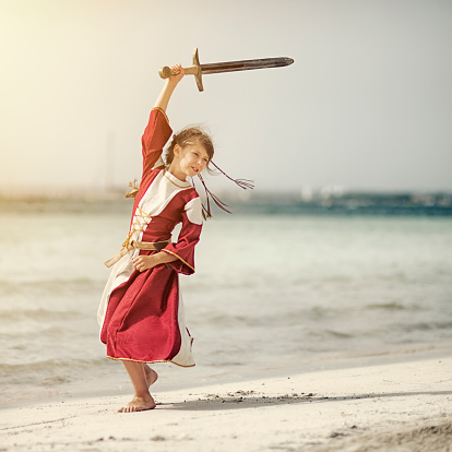 Little viking shieldmaiden practicing with sword on the beach.
