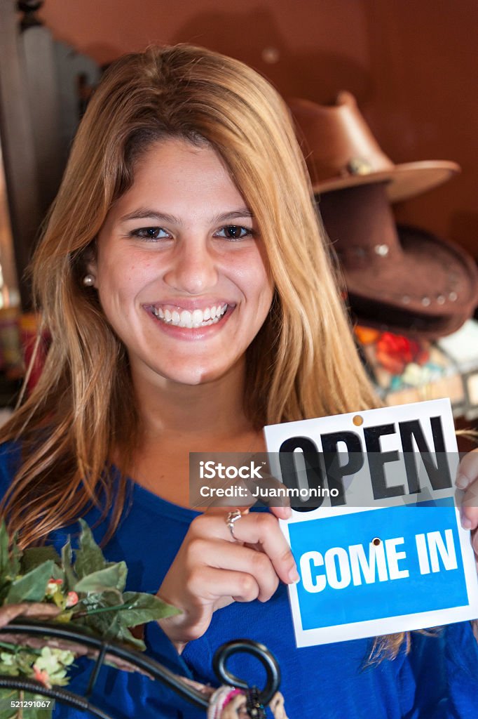 Open for business outdoors headshot of a smiling hispanic young woman holding an open sign at her gift shop 18-19 Years Stock Photo