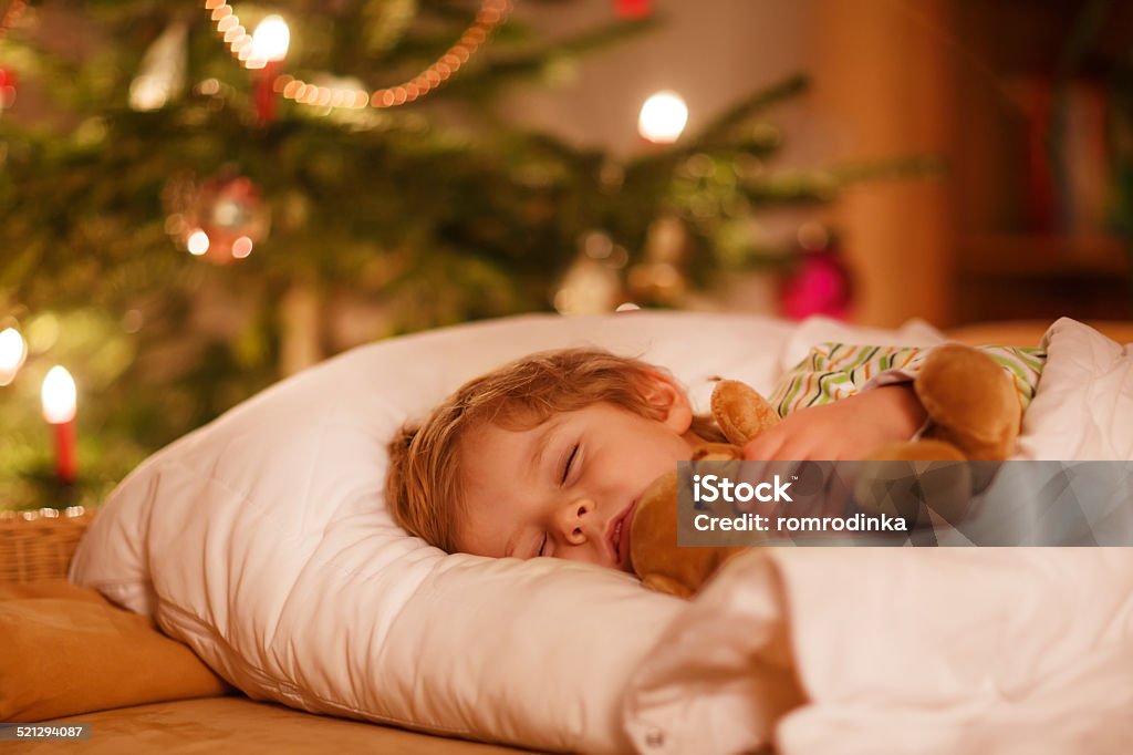 Little cute blond boy sleeping under Christmas tree Little cute blond boy sleeping under Christmas tree and dreaming of Santa at home, indoors Christmas Stock Photo