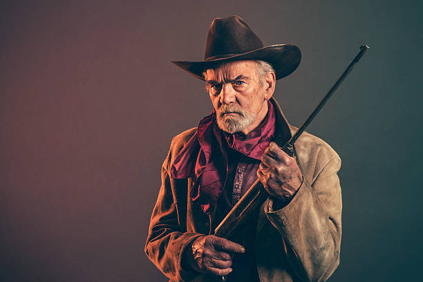 istock Senior cowboy with gray beard and brown hat holding rifle. 521315083
