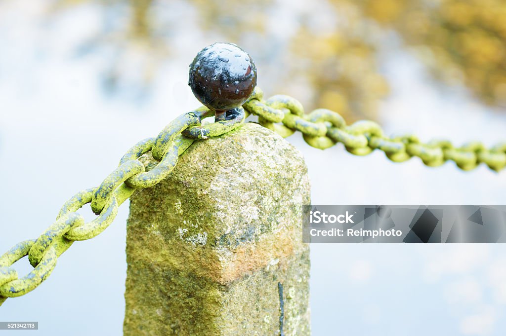 Knob on stone Black round knob on granite stone pillar with old moss covered iron chain. Water reflection out of focus in background. Reflections of sky in knob. Architectural Column Stock Photo