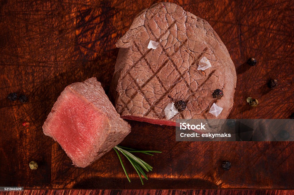 Luxurious steak. Luxurious steak background. Rare mignon beefsteak with peppercorn and rosemary herb on wooden cutting board on wooden background, top view. Culinary red meat eating. Above Stock Photo