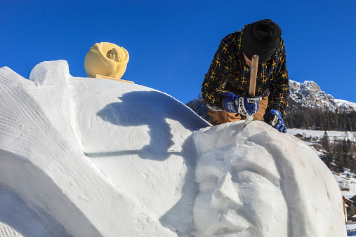 San Vigilio di Marebbe, Italy - January 20, 2010: Young man working on his snow sculpture during the annual Snow Festival. On the top stands the model to which the sculpture refers.