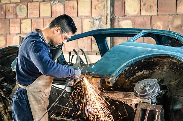Young man mechanical worker repairing and welding an old vintage car body in messy garage - Safety at work with protection wear